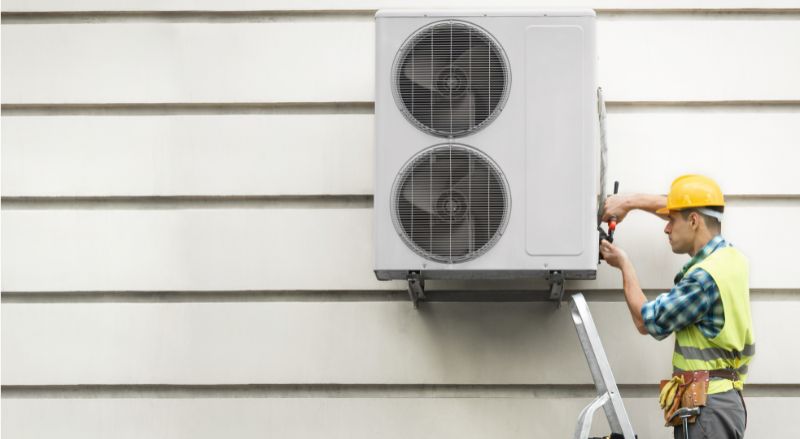 artisan en train d installer une pompe a chaleur sur une facade