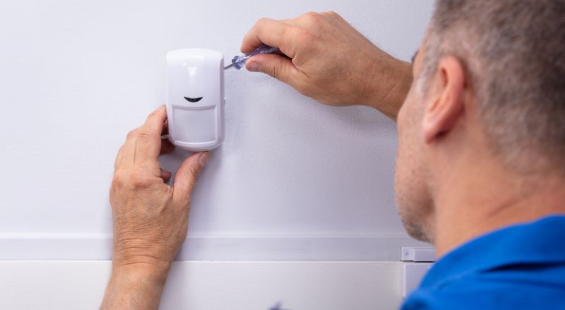 electricien installant un systeme de detecteur de mouvement sur un mur blanc