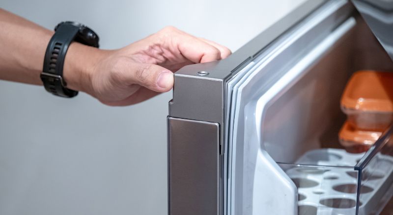 main ouvrant une porte de frigo et laissant le joint apparaitre