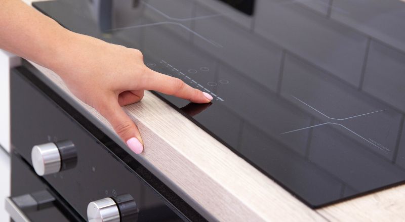 plaque vitroceramique a induction moderne avec quatre zones de cuisson une femme appuie sur la main sur l’écran tactile gros plan