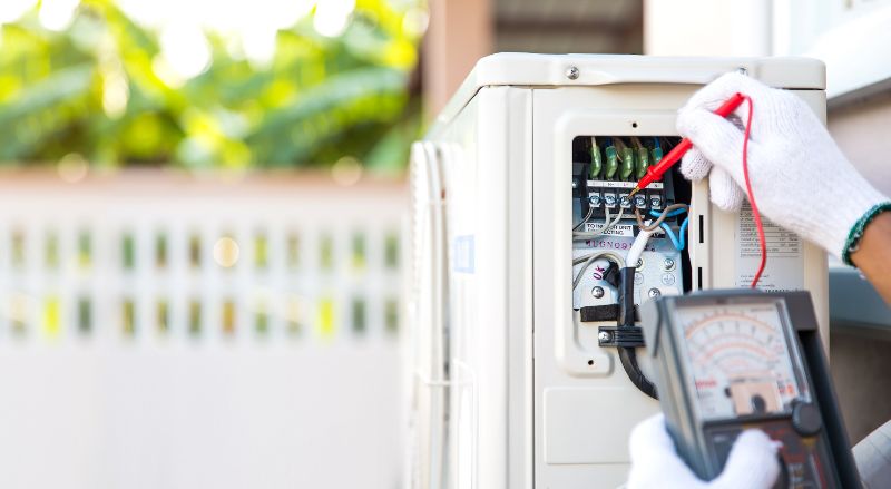 gros plan main du technicien a l aide d’un equipement de mesure verifiant la tension du courant electrique au disjoncteur sur l unité de compresseur d air exterieur apres l installation d une pompe a chaleur