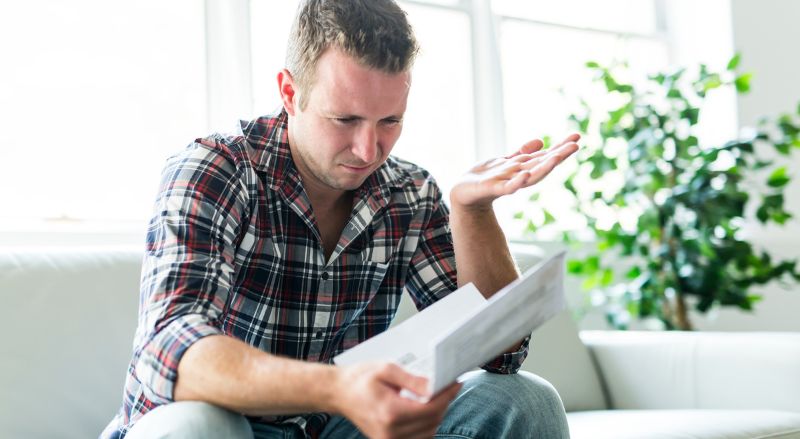 un homme exaspere tenant une facture delectricite sur son canape