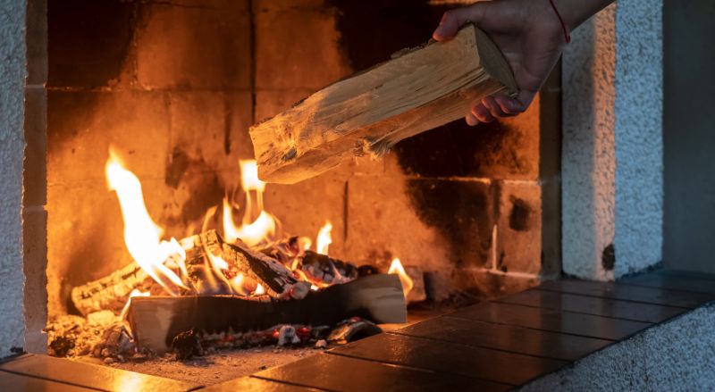des mains mettent du bois de chauffage dans une cheminee allumee par une froide journee en hiver