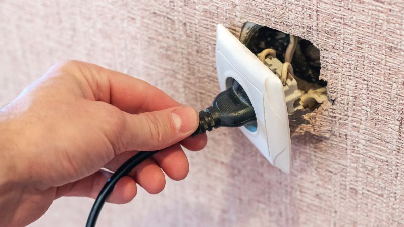 main d homme tirant sur prise electrique arrachee du mur et dangereuse