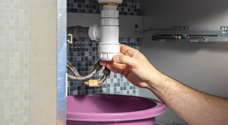 homme en train de devisser le siphon du lavabo pour enlever un gros bouchon