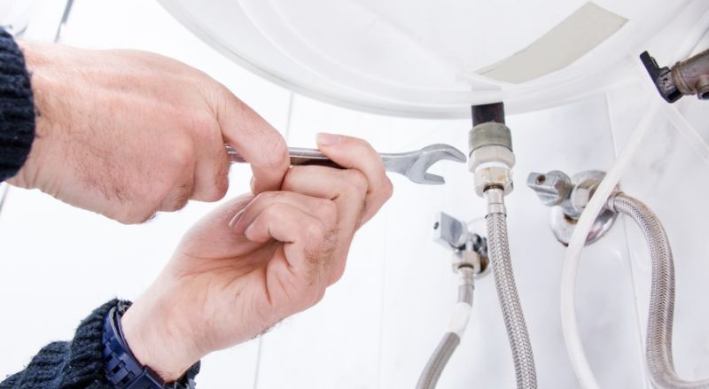 artisan en train de devisser les raccords dun chauffe eau pour le demonter