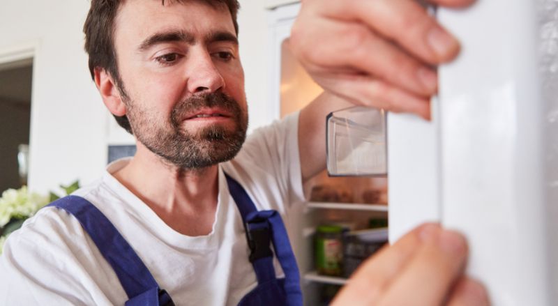 homme en bleu de travail clipsant un joint sur la porte d un frigo