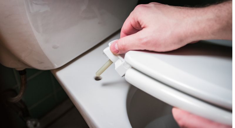 gros plan sur une main desinstallant le siege des toilettes