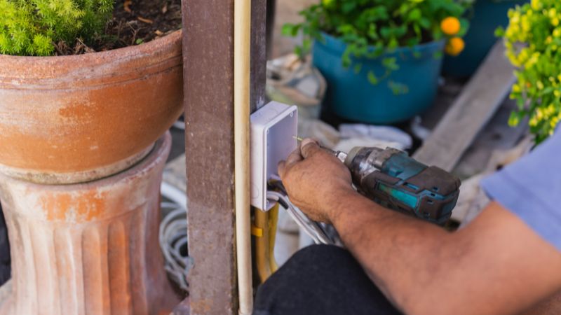 electricien installant les interrupteurs et des prises electriques sur un poteau metallique en exterieur