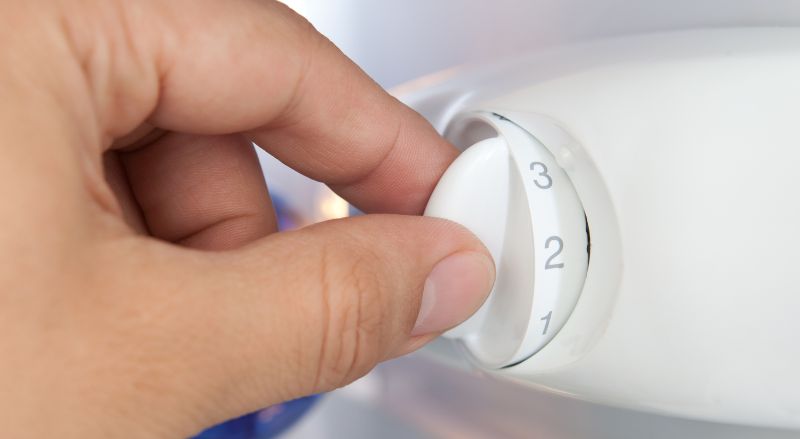 une main ajustant le thermostat d un frigo demontrant comment un simple reglage peut resoudre le probleme d une lumiere de frigo qui ne s allume plus