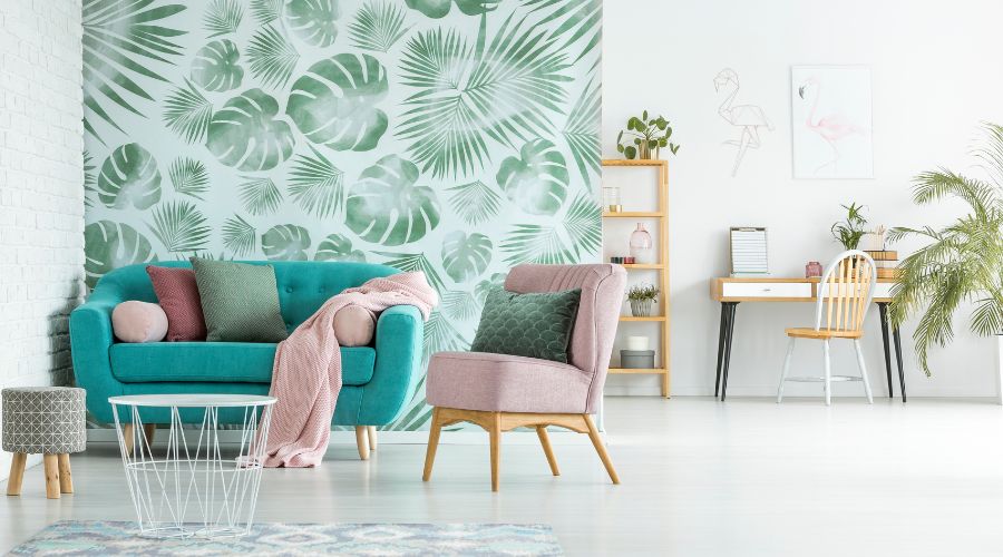 salon moderne avec un canape bleu turquoise un fauteuil rose et un pan de mur recouvert de papier peint vegetal a motifs verts sur fond blanc